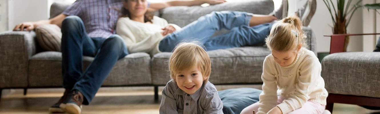 Living room with parents on the couch smiling at their kids playing