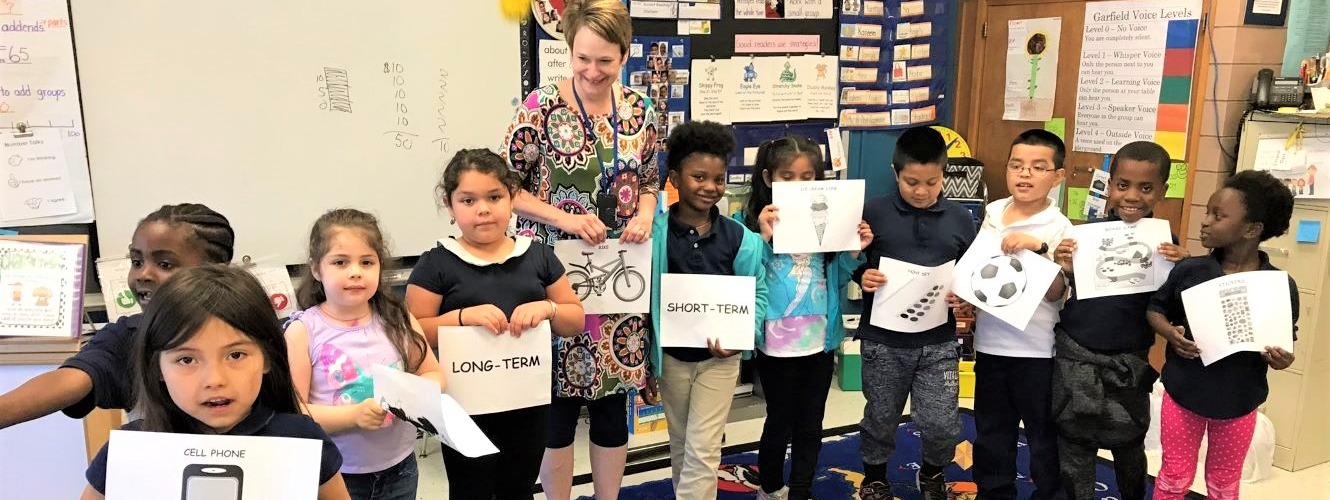 Children in a classroom holding signs with their teacher.